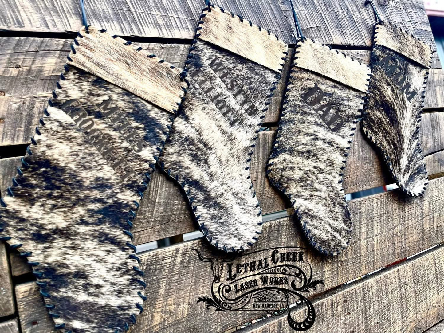 Four Christmas stockings with brindle cowhide in black, gray, and beige, hanging on a rustic wooden plank wall.