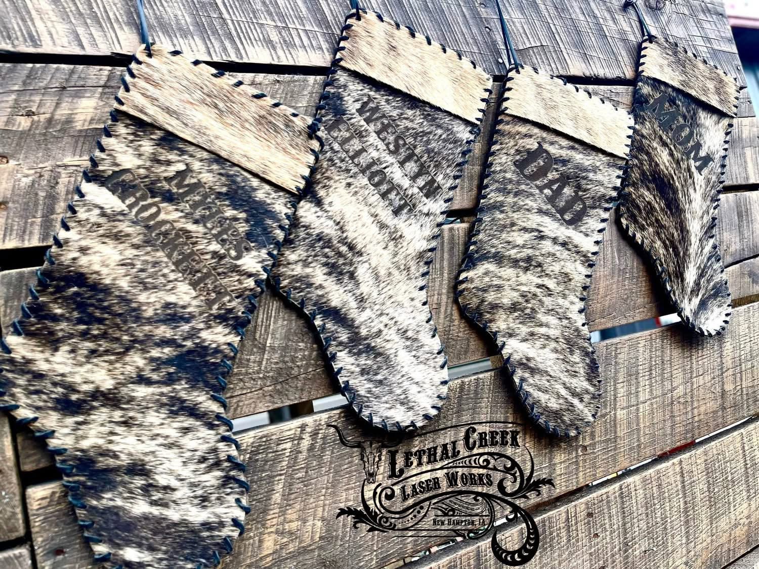 Four Christmas stockings with brindle cowhide in black, gray, and beige, hanging on a rustic wooden plank wall.