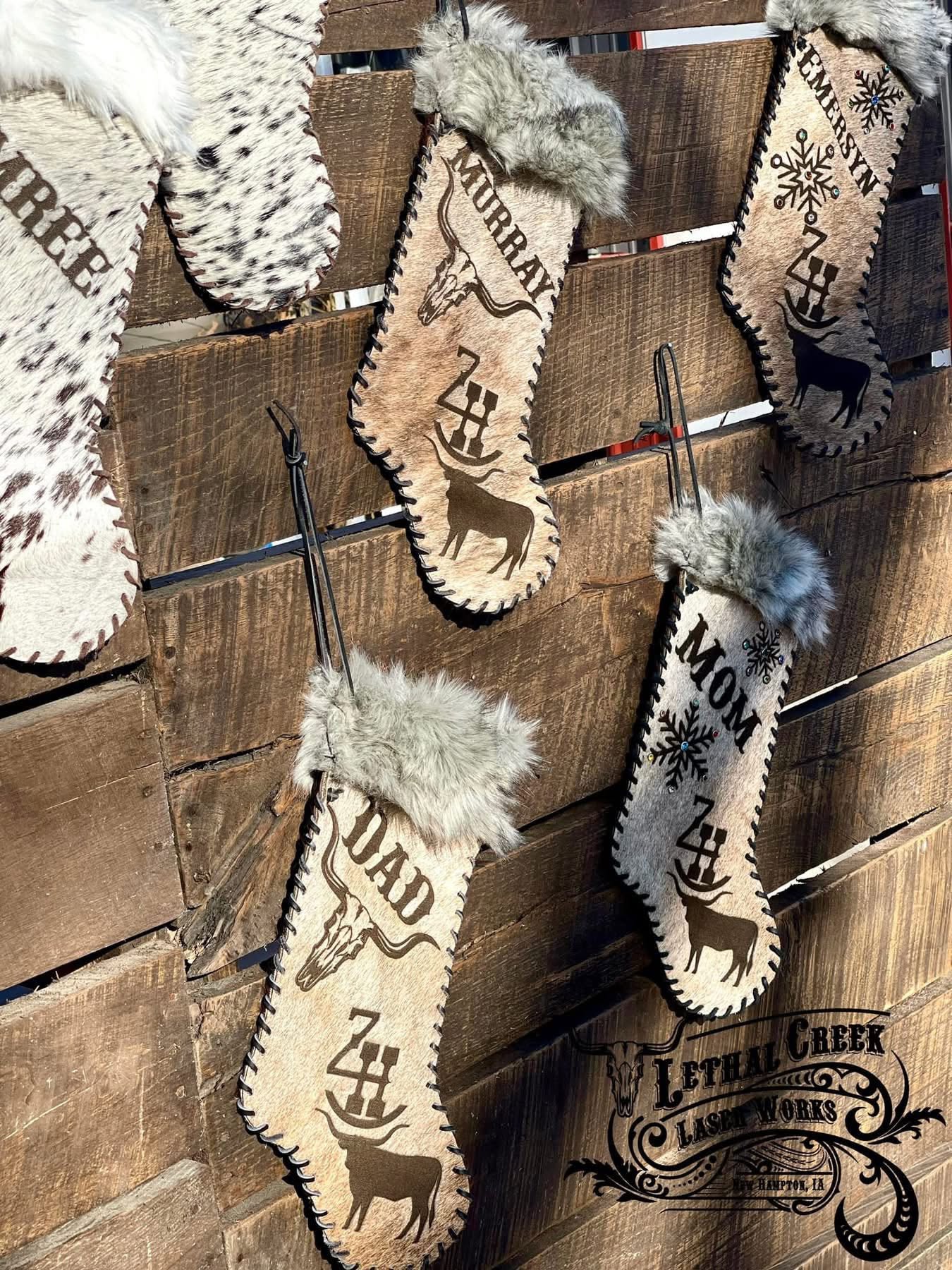 A set of rustic cowhide Christmas stockings. The stockings are made from genuine cowhide with faux fur trim, featuring custom designs including longhorn silhouettes, snowflakes, names, and cattle brand