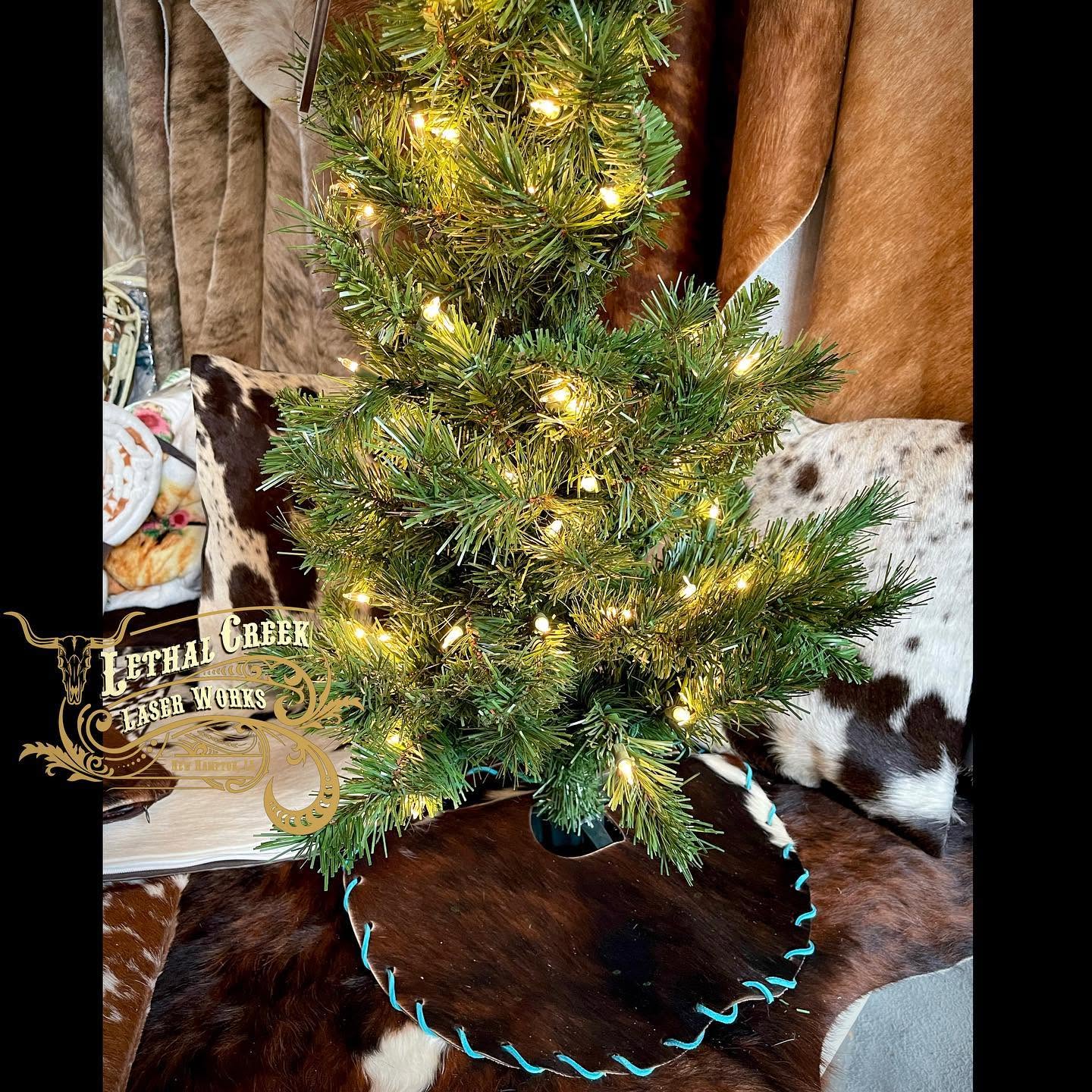 Mini cowhide Christmas tree skirt displayed under a small decorated Christmas tree